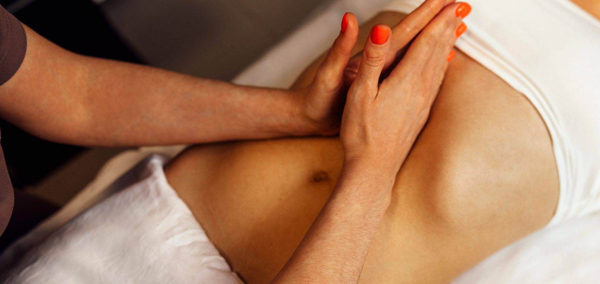 Sessão de drenagem linfática manual pelo Método Renata França, mãos de terapeuta com esmalte laranja sobre o abdômen da paciente em maca de spa, ambiente quente e relaxante, fotografia wellness profissional