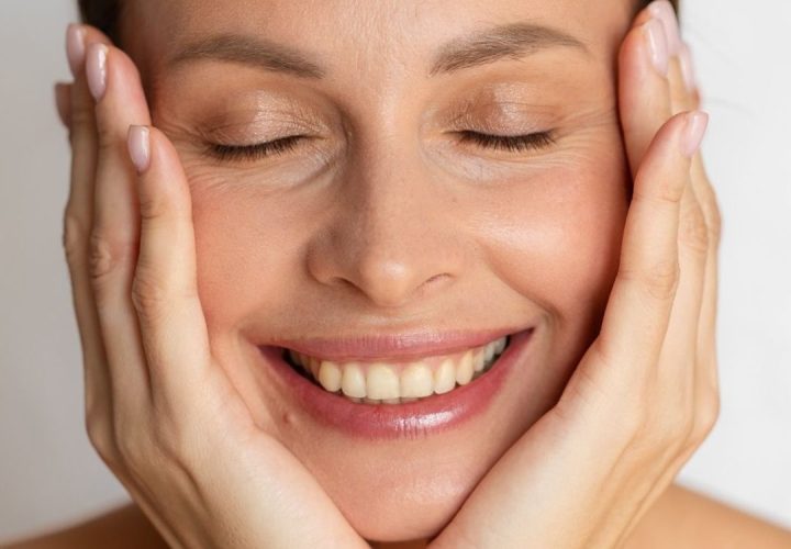 Mulher sorrindo com as mãos no rosto em imagem sobre rejuvenescimento facial natural na Bellaris Clinic